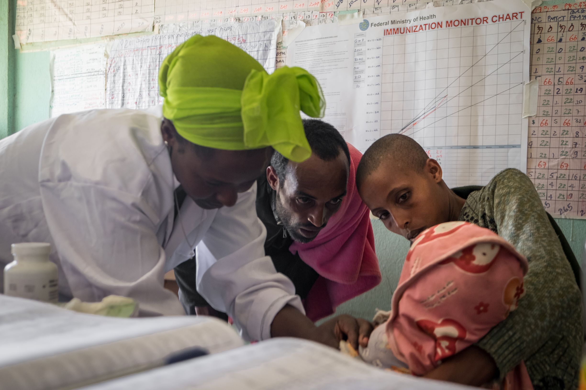 A health care worker examines a child alongside the parents. 
